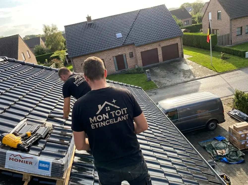Couvreur de dos en t-shirt Mon Toit Étincelant sur une toiture en tuiles noires, cloueur et palette de tuiles à côté
